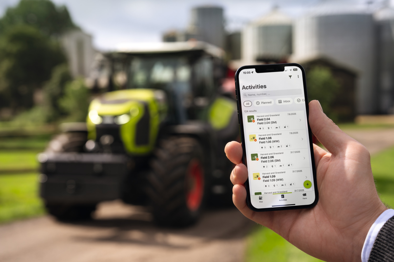 Mobiltelefon med arbeidsoversikt i CLAAS connect foran en traktor