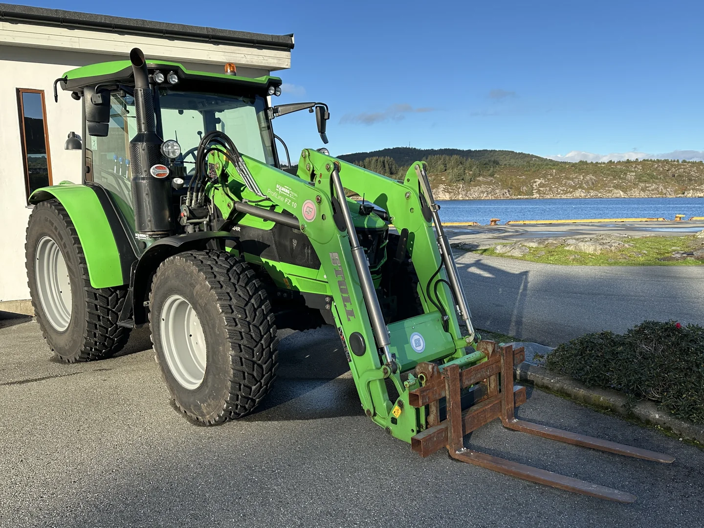 Grønn Deutz-Fahr med STOLL frontlaster og pallegaffel ved sjøen i Bekkjarvik
