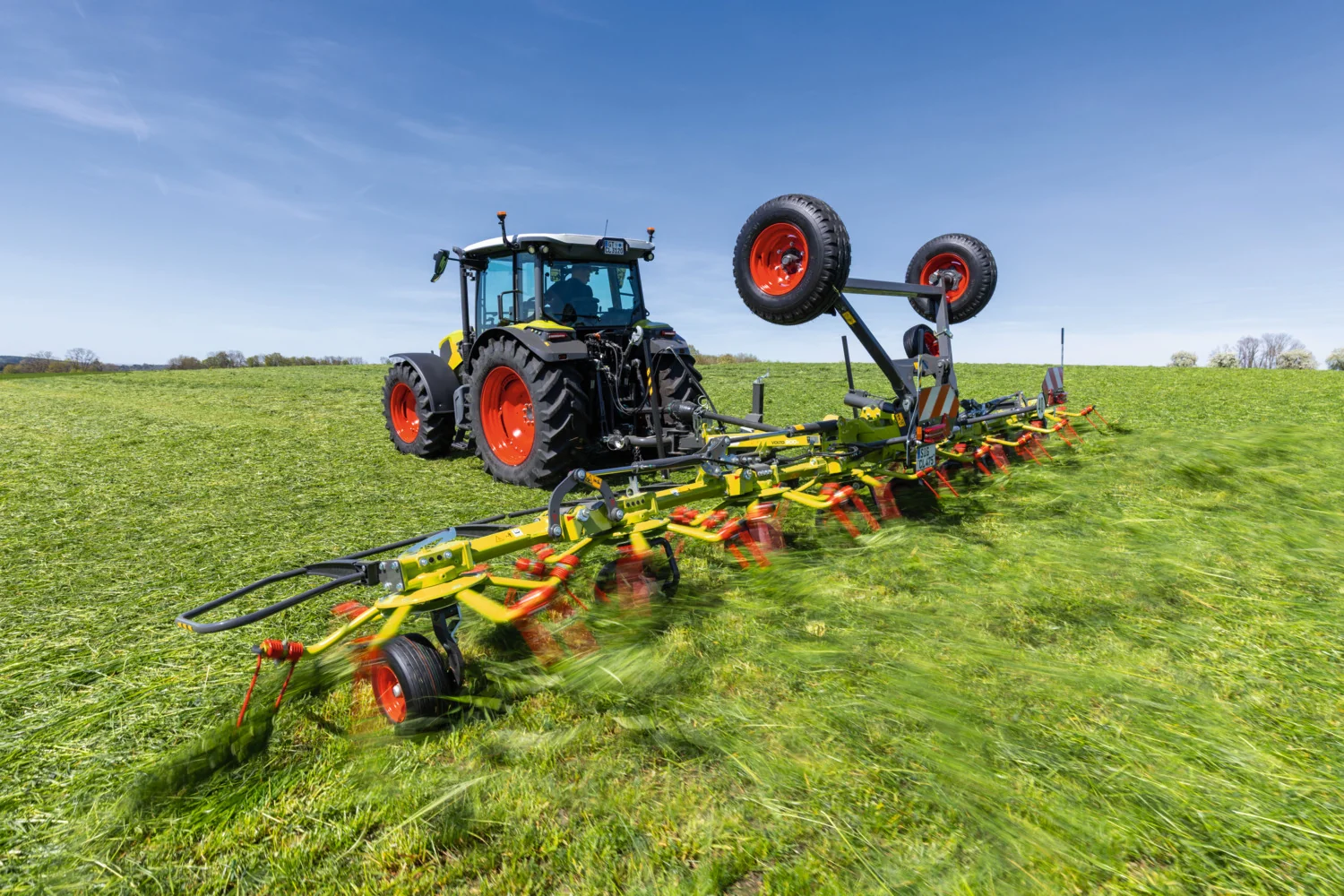 CLAAS-traktor med en VOLTO-grasvender på et slått jorde