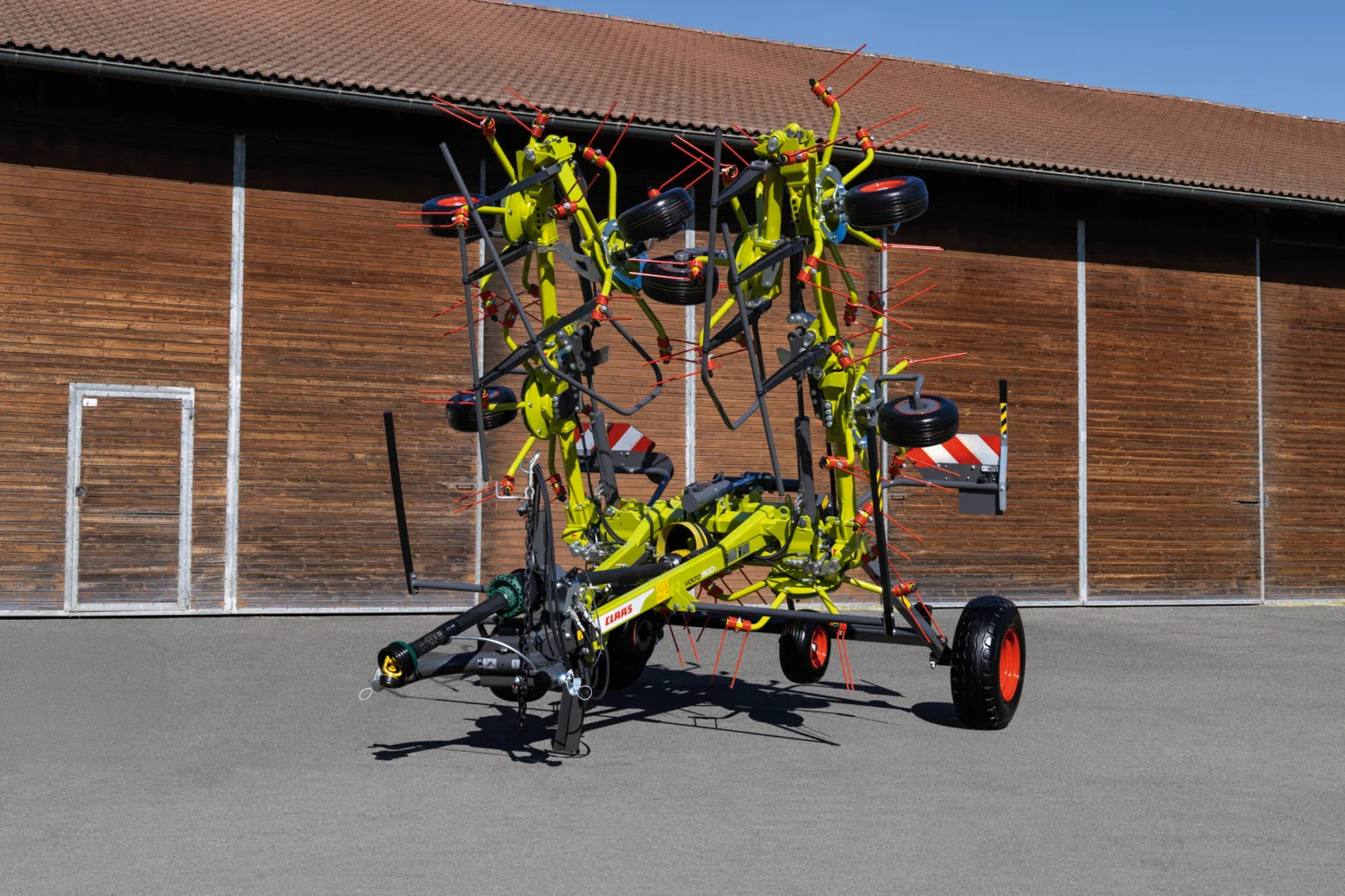 Sammenfoldet CLAAS VOLTO-grasvender med transporthjul ved en maskinhall