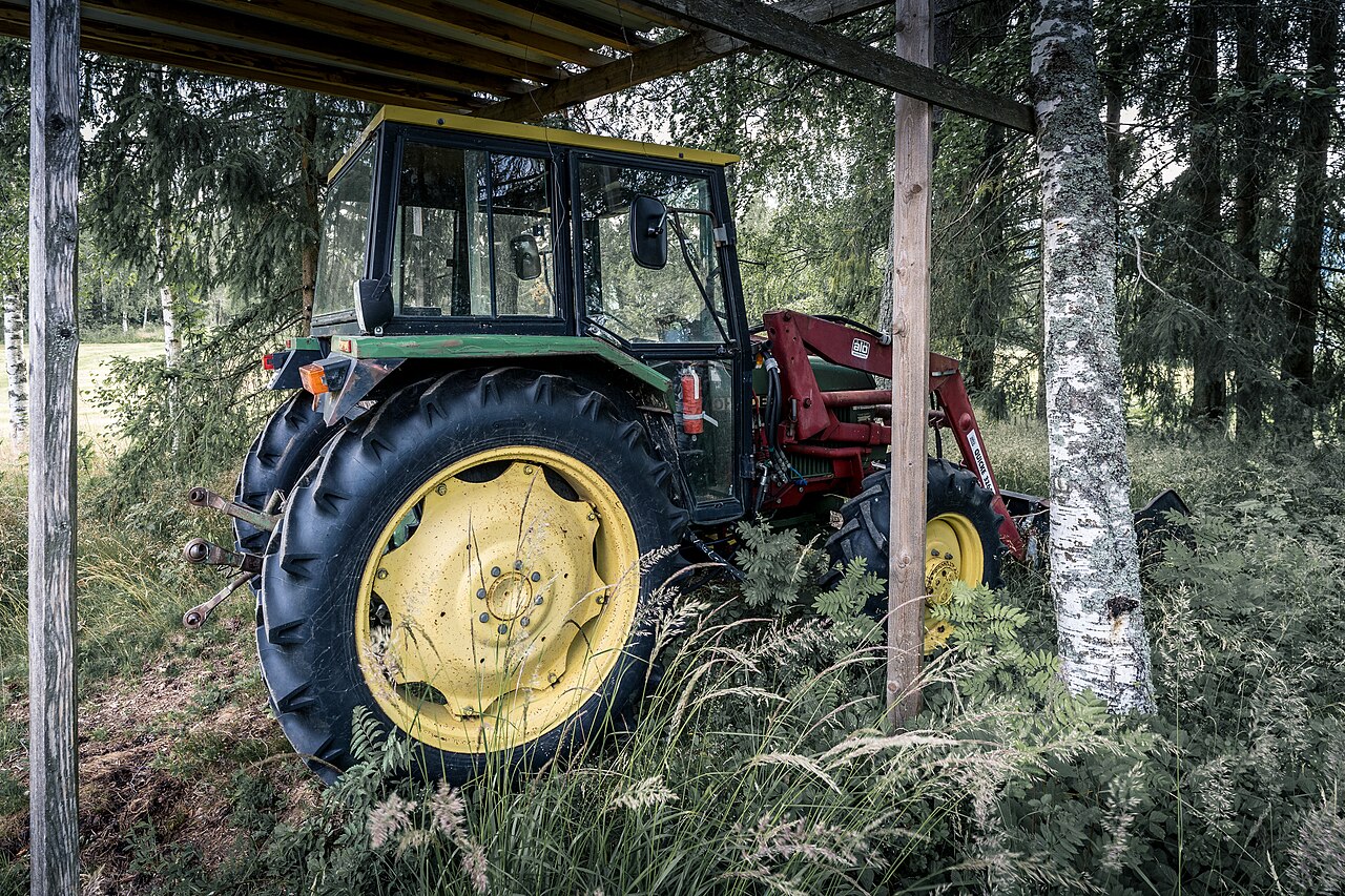Eldre John Deere med frontlaster parkert under et overbygg på Grue gård i Hurdal