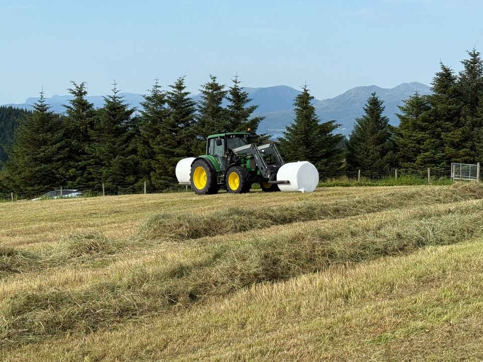 John Deere med frontlaster og hvit rundball på et grasjorde på Vestlandet