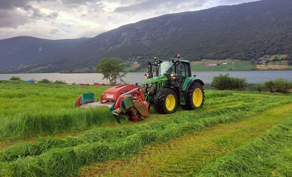 John Deere 6M 125 med Kverneland-slåmaskin i en eng i Lom