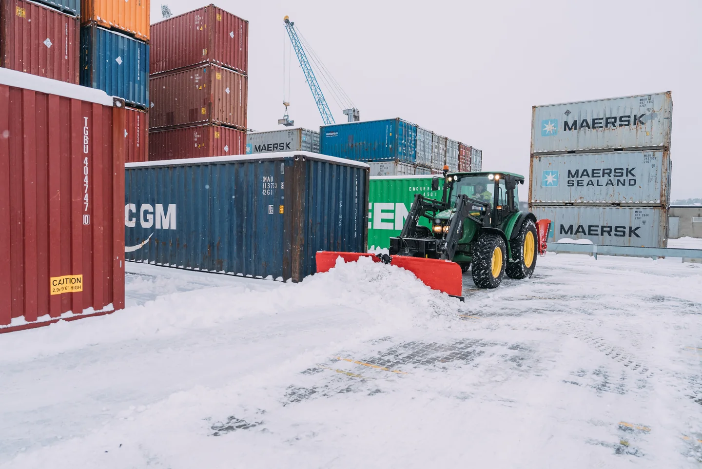 Grønn traktor med rød Tokvam VT CITY-plog rydder en plass ved containere