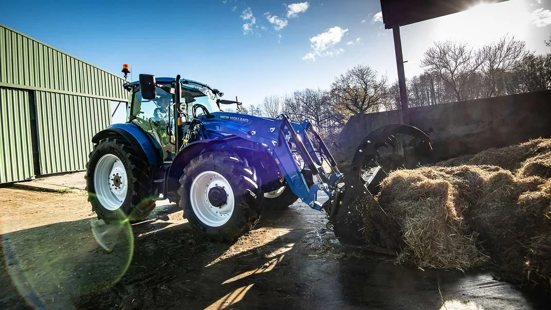 New Holland T5 Dual Command med frontlaster i arbeid ved et gårdsbygg