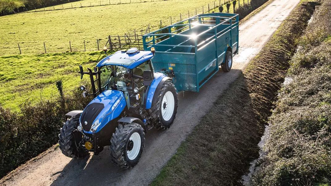 New Holland T5 Dual Command med tilhenger på en gårdsvei
