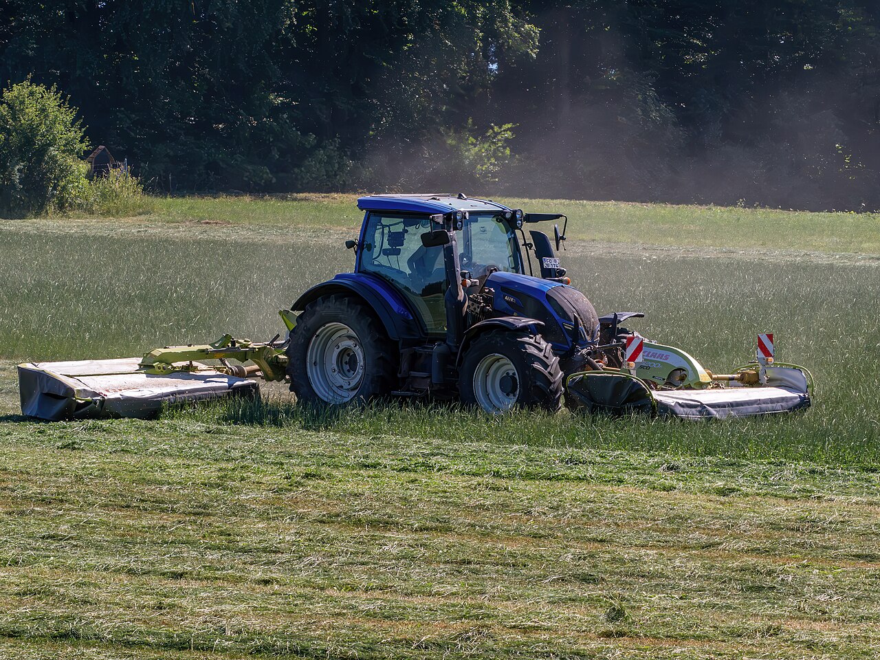 Blå Valtra G135 med slåmaskiner på en eng